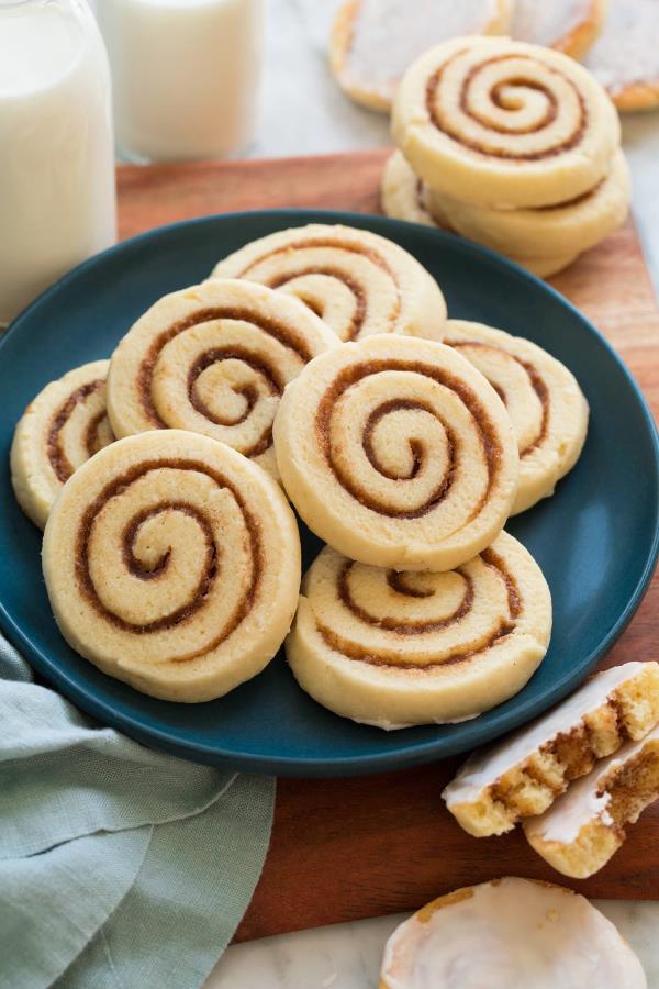 Cinnamon roll coo<em></em>kies piled on a blue plate on a wooden surface.