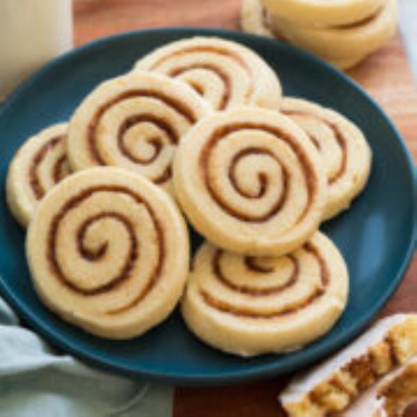 Cinnamon roll coo<em></em>kies piled on a blue plate on a wooden surface.