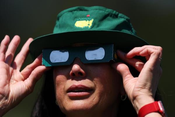 A patron uses glasses to view the eclipse during a practice round prior to the 2024 Masters Tournament at Augusta Natio<em></em>nal Golf Club.