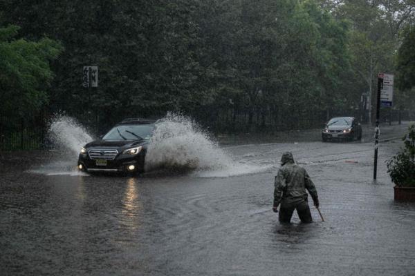 A man clears debris from a drain as a car make their way through floodwater in Brooklyn, New York on September 29, 2023. (Photo by Ed Jo<em></em>nES / AFP) (Photo by ED JONES/AFP via Getty Images)